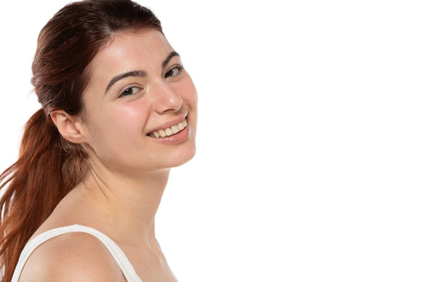 una joven pelirroja sonriente sin maquillaje con el pelo largo sobre un fondo de estudio blanco - Foto, imagen