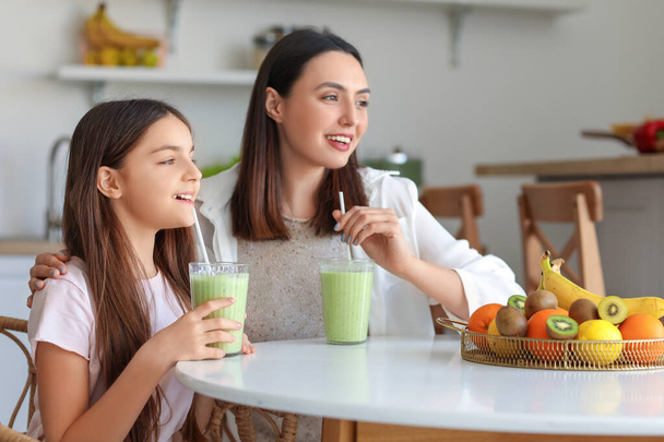 Bambina con sua madre che beve frullato verde a tavola in cucina - Foto, immagini
