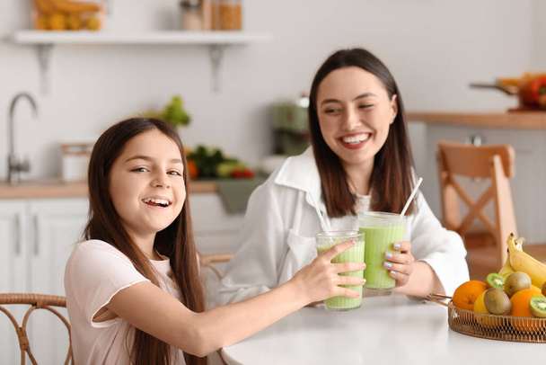 Niña con su madre bebiendo batido verde en la mesa en la cocina - Foto, Imagen
