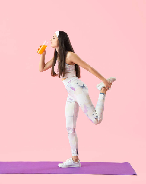 Sportowa młoda kobieta ze szklanką soku warzywnego trening na różowym tle - Zdjęcie, obraz