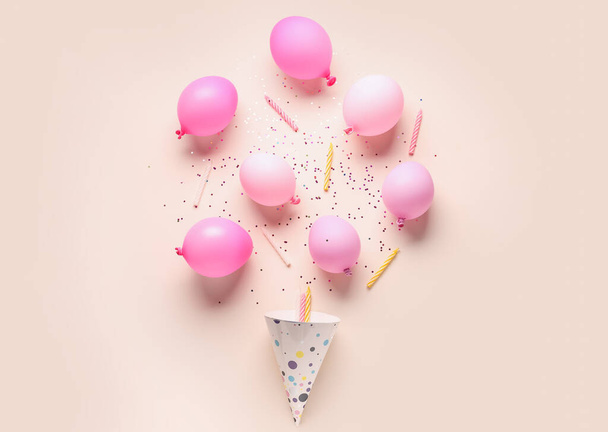 Party-Hut mit Luftballons und Kerzen auf hellorangefarbenem Hintergrund - Foto, Bild
