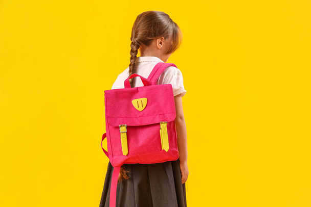 Kleines Schulmädchen mit Rucksack auf gelbem Hintergrund, Rückseite - Foto, Bild