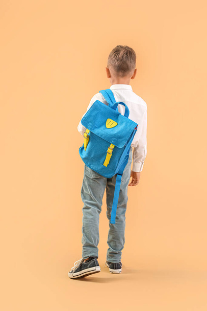 Маленький школяр з блакитним рюкзаком на помаранчевому фоні, вид ззаду - Фото, зображення