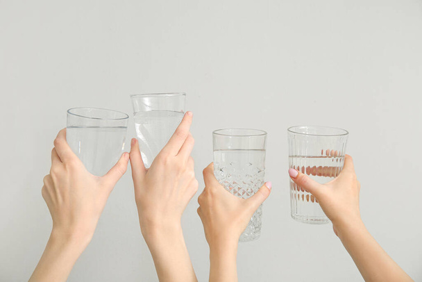 Weibliche Hände mit Gläsern kalten Wassers auf hellem Hintergrund - Foto, Bild
