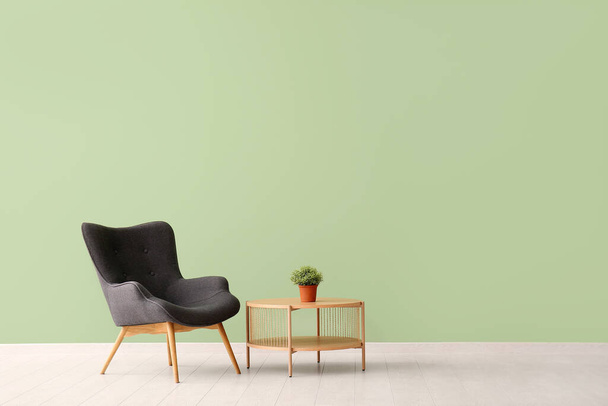Grauer Sessel und Zimmerpflanze auf Couchtisch neben grüner Wand - Foto, Bild
