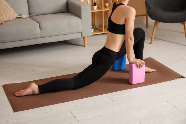 Giovane donna sportiva che pratica yoga con blocchi a casa - Foto, immagini