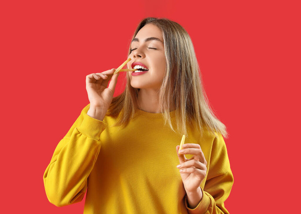 Όμορφη νεαρή γυναίκα τρώει τηγανητές πατάτες σε κόκκινο φόντο - Φωτογραφία, εικόνα