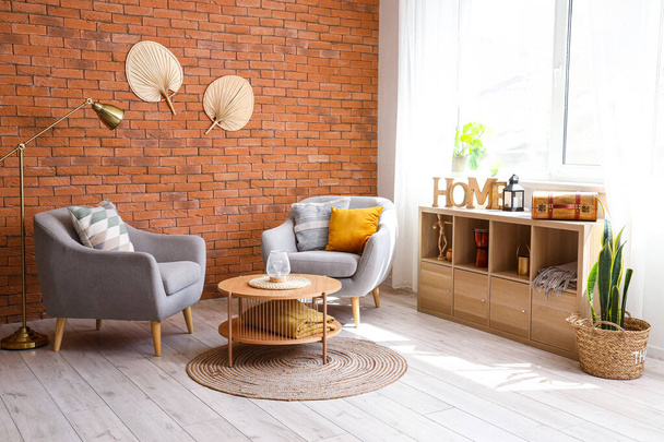 Stijlvolle grijze fauteuils, salontafel en plank in de buurt van raam in lichte woonkamer - Foto, afbeelding