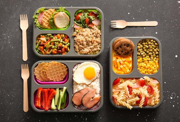 Багато обідніх коробок з різними смачними стравами на гранжевому чорному фоні - Фото, зображення