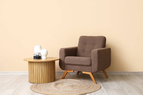 Стильне коричневе крісло та дерев'яний журнальний столик біля бежевої стіни - Фото, зображення
