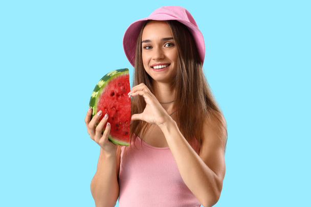 Young woman with fresh watermelon making heart gesture on blue background - Photo, Image