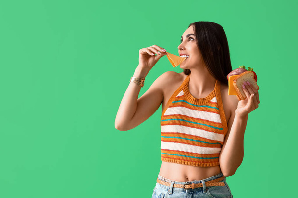 Νεαρή γυναίκα τρώει νόστιμο σάντουιτς σε πράσινο φόντο - Φωτογραφία, εικόνα