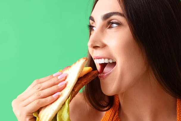 緑の背景で美味しいサンドイッチを食べる若い女性, クローズアップ - 写真・画像