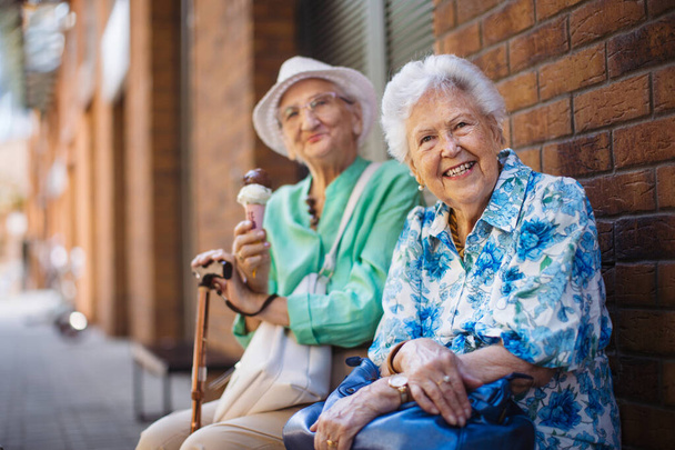 Portrait of two senior female friends in the city, eating ice cream on a hot summer day. Elderly ladies on summer vacation in the city. Pensioners on group trip. Concept of senior vacation and travel - Fotoğraf, Görsel