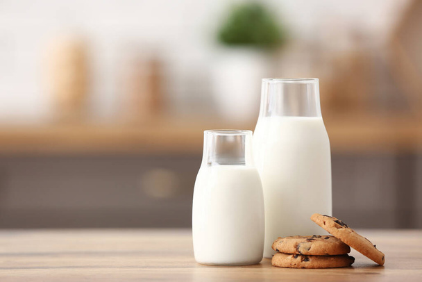 Flessen verse melk met zoete koekjes op houten tafel in de keuken - Foto, afbeelding