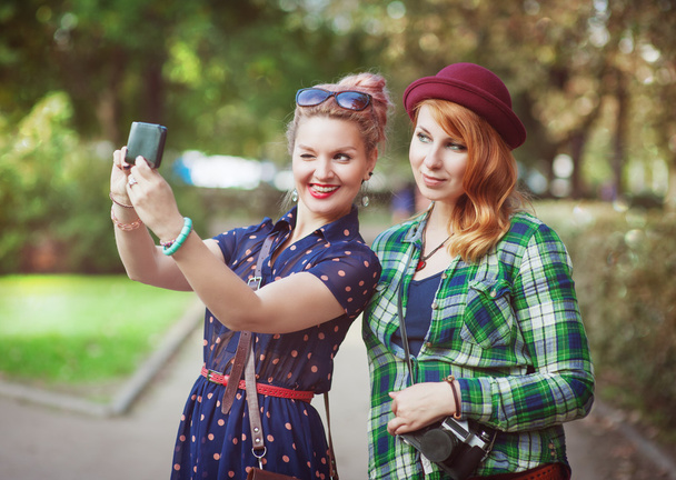 Deux filles hipster avec bretelles prenant des photos d'elles-mêmes sur m
 - Photo, image