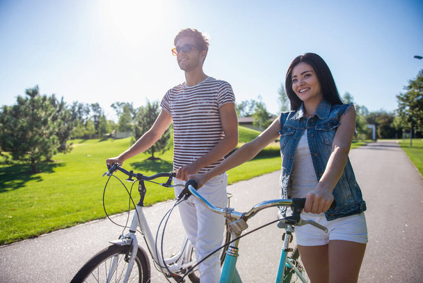 Красива пара з нетерпінням чекає і посміхається під час їзди на велосипеді в парку
 - Фото, зображення