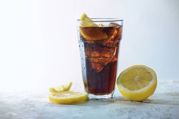 Fresh cola with ice cubes and lemon slices in a drinking glass against a light blue gray background, refreshing sweet caffeine drink, copy space, selected focus, narrow depth of field - Photo, image