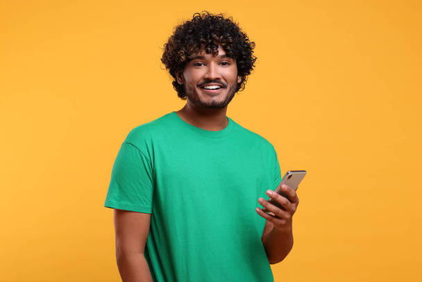 Handsome smiling man using smartphone on yellow background - Foto, afbeelding