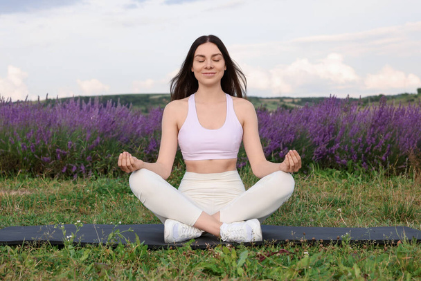 Glimlachende vrouw oefenen yoga in de buurt van lavendel buiten - Foto, afbeelding