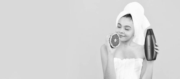 Mädchen mit gesunder Haut, Gesichtsbehandlung, lächelndes Teenie-Mädchen im Handtuch mit Grapefruit-Shampoo-Flasche auf gelbem Hintergrund. Kosmetik und Hautpflege für Teenager, Plakatgestaltung - Foto, Bild