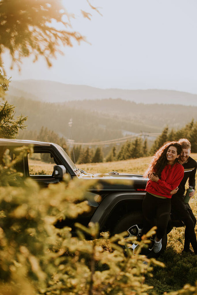 Όμορφο νεαρό ζευγάρι χαλαρώνοντας από ένα όχημα εδάφους κουκούλα στην ύπαιθρο - Φωτογραφία, εικόνα