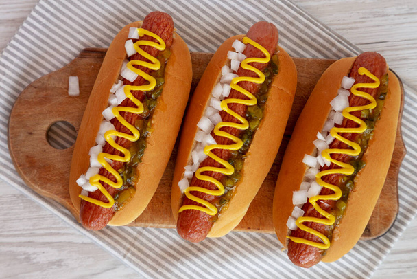 Hot Dog grillé à l'omble avec moutarde, relish et oignon sur une planche en bois rustique, vue sur le dessus.  - Photo, image