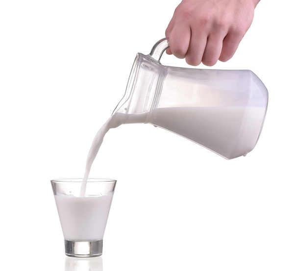 Melk van kruik fles in een glas gieten op witte achtergrond - Foto, afbeelding