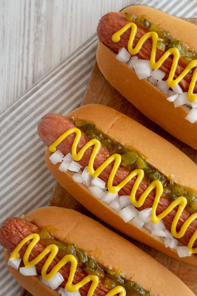 Saibling-Hot-Dog mit Senf, Relish und Zwiebeln auf rustikalem Holzbrett, Draufsicht.  - Foto, Bild