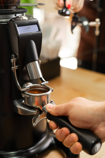 Vers gemalen koffie van een moderne professionele koffiemolen valt in een dubbele portafilter. Het proces van het maken van espresso koffie in de coffeeshop. Close-up - Foto, afbeelding