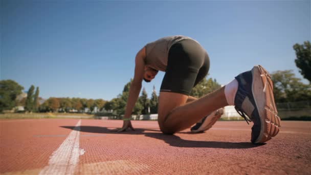 Slow motion of male athlet starting to run by the runway. Young sportsman beginning to run from the set position. Caucasian fit guy running away by the runway at the stadium - Footage, Video
