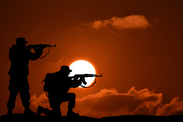 Silhueta de dois soldados militares ou oficial com armas ao pôr-do-sol. tiro, segurando arma, céu colorido, montanha, fundo, equipe
 - Foto, Imagem