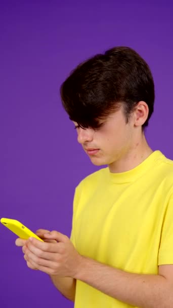 Genç çocuk, mor arka planda izole edilmiş bir telefonla sesli mesaj ya da sesli mesaj gönderiyor. - Video, Çekim