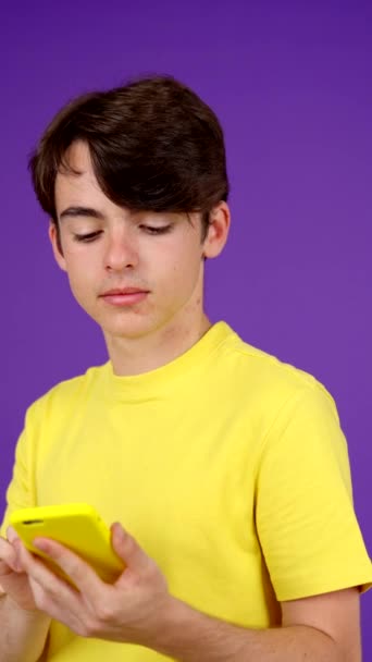 Emotional teenager boy listening voice message on phone isolated on purple background. - Footage, Video