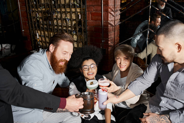 radośni, wieloetniczni koledzy wznoszący toast napojami alkoholowymi w barze koktajlowym, rozrywkowym i rozrywkowym - Zdjęcie, obraz
