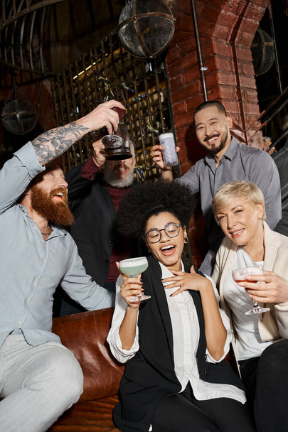 bearded tattooed men toasting near carefree women in cocktail bar, relax of multiethnic colleagues - Fotoğraf, Görsel
