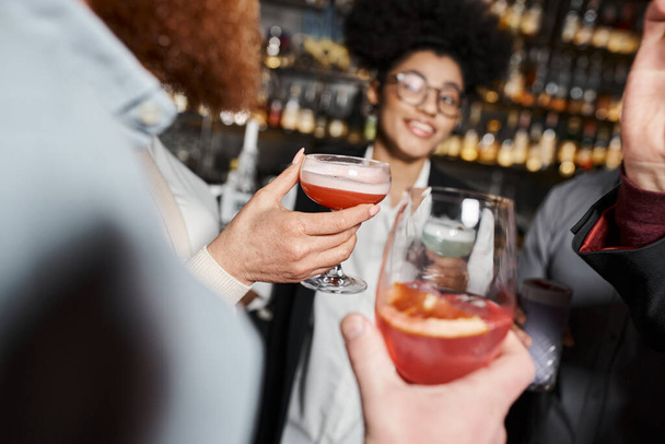 happy african american woman near colleagues with cocktail glasses in bar, blurred background - Foto, Imagem