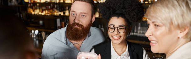удивленный бородатый мужчина рядом с веселыми мультиэтнических женщин, проводящих после рабочего времени в коктейль-баре - Фото, изображение
