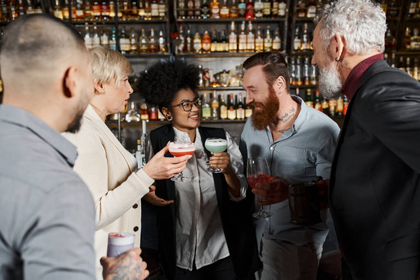 мультиэтнические коллеги с напитками, улыбающимися во время беседы в баре, досуг разнообразной команды - Фото, изображение
