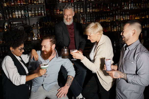 vidám szakállas férfi és afro-amerikai nő nevet közelében multietnikus kollégák a bárban - Fotó, kép