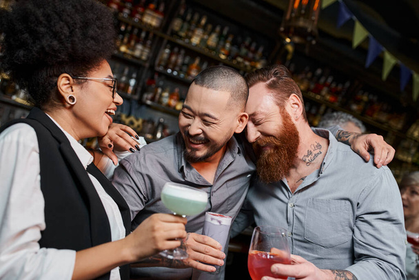 homens barbudos e mulher afro-americana rindo em bar de coquetéis, lazer de colegas multiétnicos - Foto, Imagem