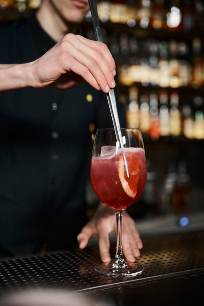 vista recortada del camarero añadiendo rodaja de naranja fresca en cóctel de alcohol en el bar, creación de bebidas - Foto, imagen