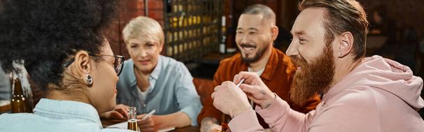 позитивний бородатий чоловік розмовляє з різноманітною багатоетнічною командою під час зустрічі в пабі після роботи, банер - Фото, зображення