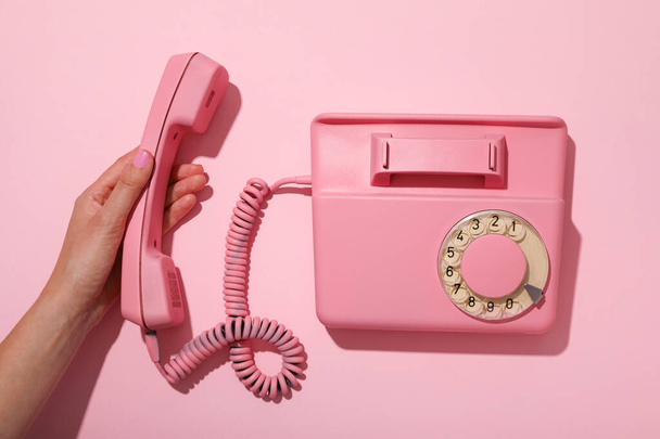 Vintage roze telefoon en vrouwelijke hand op roze achtergrond, bovenaanzicht - Foto, afbeelding