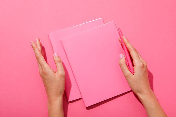 Σημειωματάρια, στυλό και γυναικεία χέρια σε ροζ φόντο, πάνω όψη - Φωτογραφία, εικόνα