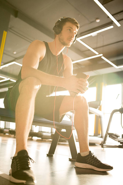 Young muscular man in sportswear sitting and listening to music in sport club - Fotoğraf, Görsel