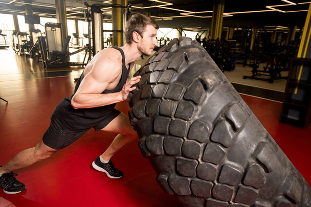 Strong muscular man working out with a huge tire, he raising and carrying it in gym - Fotografie, Obrázek