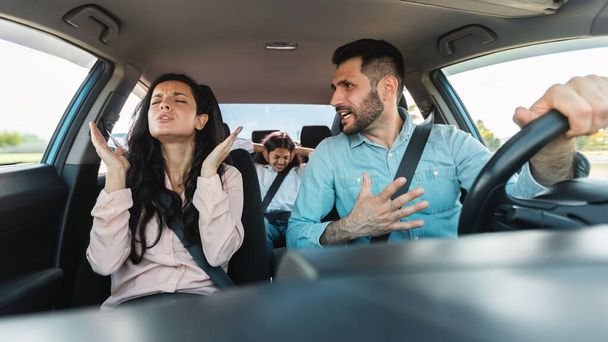Fiatal család veszekednek az autóban, férj kiabál feleséggel vezetés közben, gyerek lány ül a hátsó ülésen és csukott fülekkel. Házassági válság, házastársak közötti konfliktus - Fotó, kép