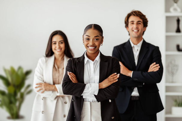 Successful black businesswoman standing with folded arms in front of her business team posing in office and smiling at camera. Entrepreneurship and leadership concept - Photo, Image