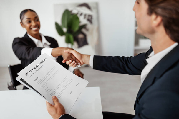 Succesvol sollicitatiegesprek. ingehuurde zwarte vrouwelijke kandidaat bezegelt de deal met het HR-team recruiter door handdruk na het ondertekenen van arbeidscontract - Foto, afbeelding